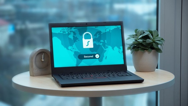 Laptop showing a security padlock on screen on a small round table next to a plant and a clock