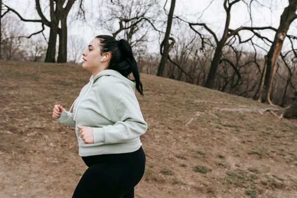 Young woman in a light hoodie jogging through a park on a cool autumn day
